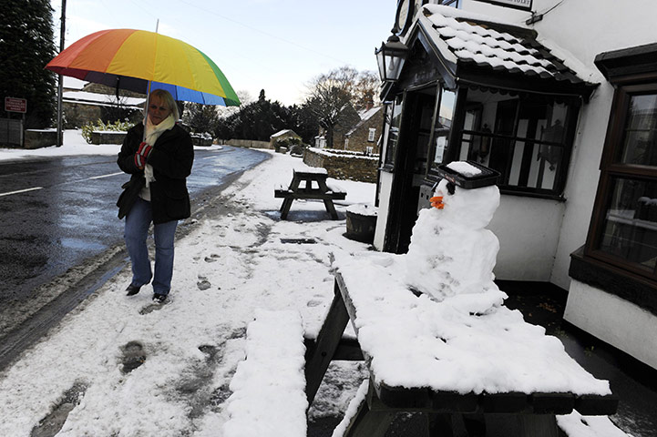 Snow: winter Weather: A woman walks past a snowman in the street at Sutton-Under-Whitestonecliffe