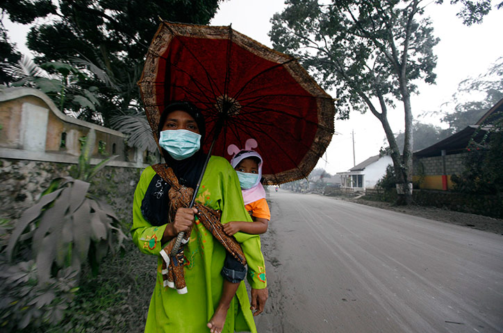 24 hours in pictures: A mother carries her child as she walks down an ash-covered street