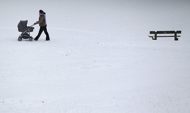 Snow today: A woman pushes a pram through the snow in Bramall Park in Manchester