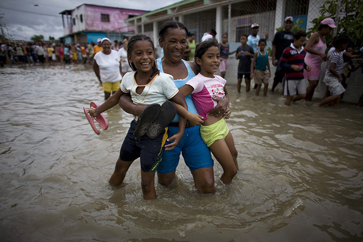 Venezuela floods: A woman carries two girls through a flooded street in Higuerote, Venezuela