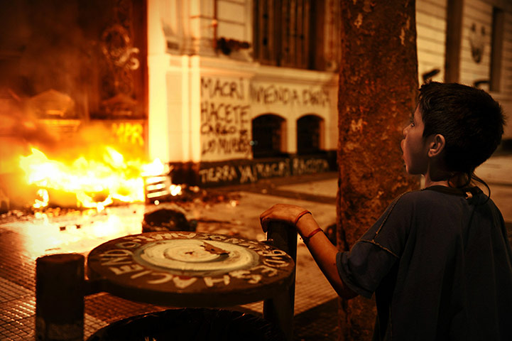 24 Hours in Pictures: A boy watches a fire set by masked activists in Buenos Aires