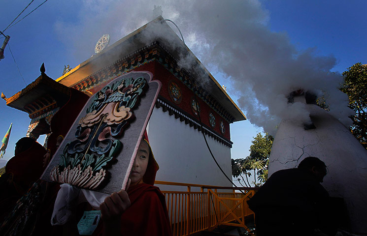24 hours in pictures: A young Tibetan monk holds a board with carvings on it as smoke rises