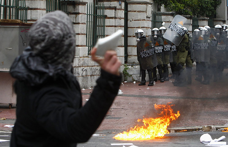 Riots in Athens: A protester throws a rock at riot policemen during protests in Athens