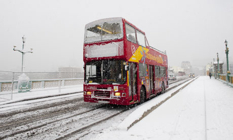 A sightseeing tour bus on Southwark bridge, London in a snowstorm.