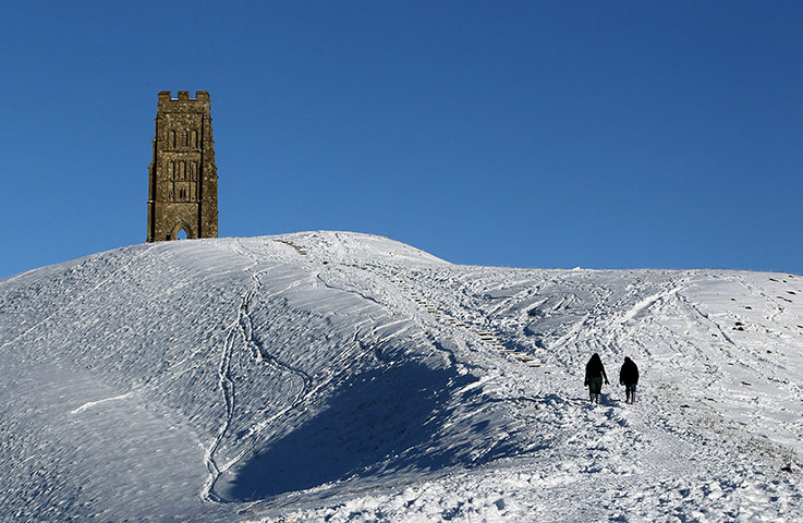 Cold weather continues:  A couple walk in the snow below Glastonbury Tor in Somerset