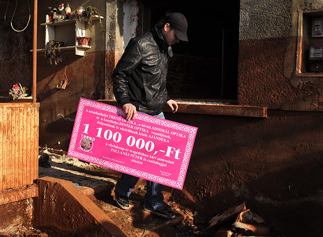 24 hours: Devecser, Hungary: A victim of toxic red sludge holds a symbolic cheque