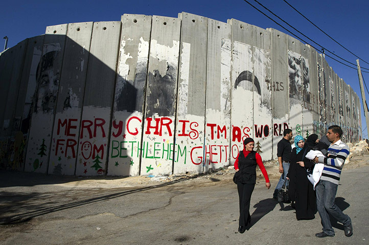 Christian in Middle East: Palestinians walk past a Christmas greeting painted on separation barrier