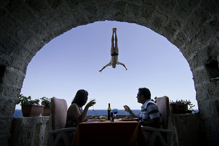 2010: year in pictures: Lunchers watch a cliff-diver in Polignano a Mare, Italy