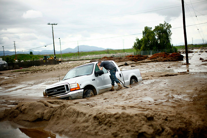 24 hours in pictures: S A resident checks inside a vehicle stuck in the mud after flood