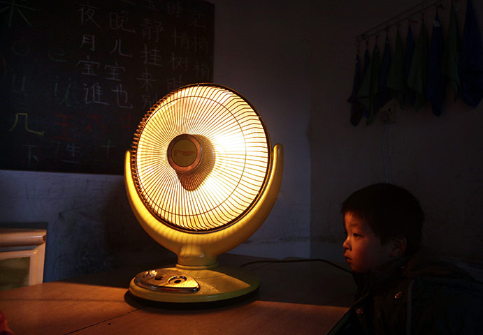 24 hours : Beijing, China: A boy sits next to an electric heating fan in a classroom