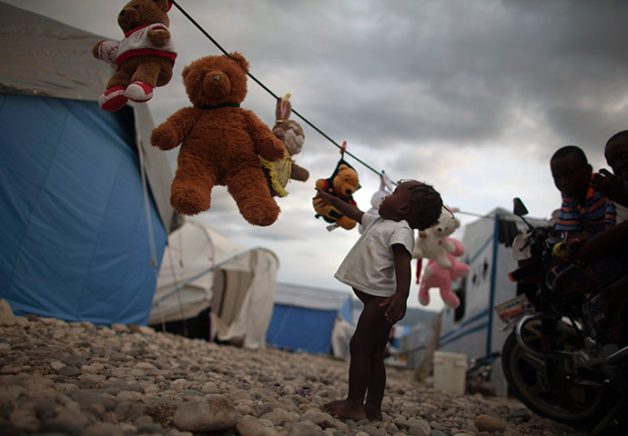 24 hours in pictures: A child reaches out for a stuffed animal hanging to dry at Caradeux Camp