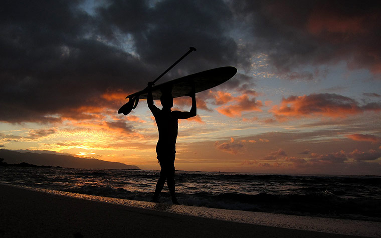 24 hours in pictures: Waialua,Hawaii: A surfer holds his board aloft as the sun sets