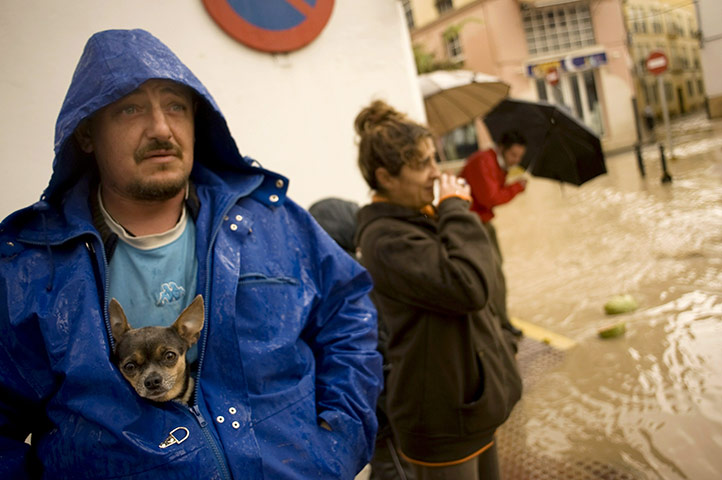 24 hours: Ecija, Spain: A man and his dog stand in a flooded street 
