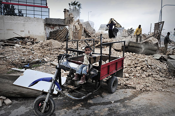 24 Hours in Pictures: A young boy sits in a hand made vehicle in Athens