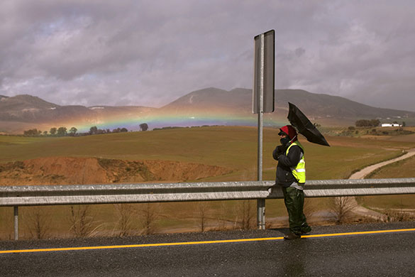 24 hours in pictures: Canete La Real, Spain: A road worker holds an umbrella during rain