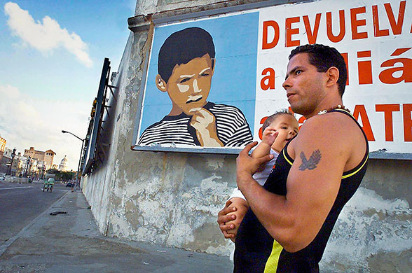 Elian Timeline: A Cuban man walks with a baby in Havana past a poster of Elian Gonzalez