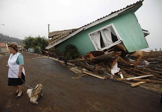 chile update: A woman stands in front of a damaged house in Pelluhue, Chile