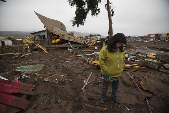 Chile earthquake: A woman stands in front of a damaged house in Pelluhue