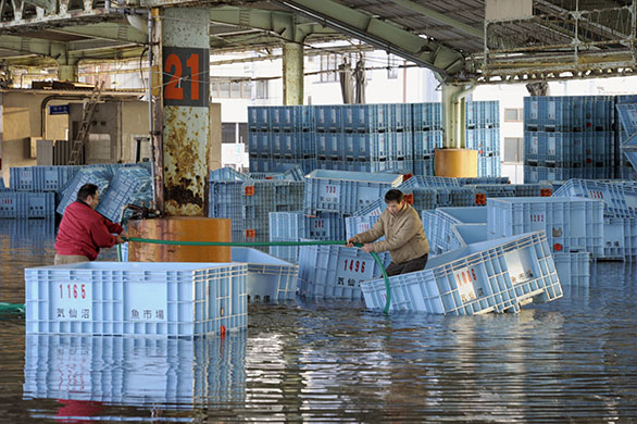 Tsunami damage: Workers retrieve containers at a flooded fish market in Kesennuma, Japan 