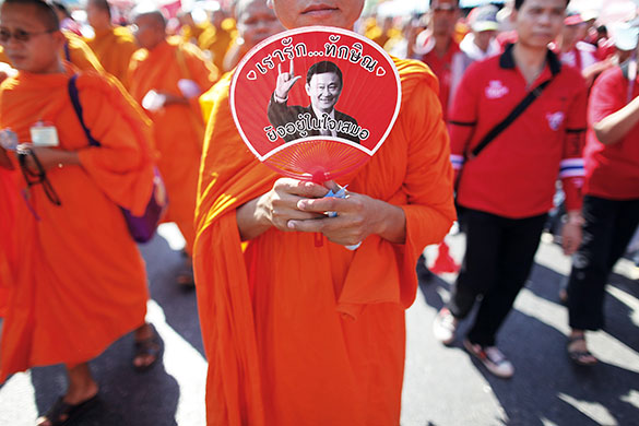 Thailand protests: A Buddhist monk holds a fan with a picture of Shinawatra