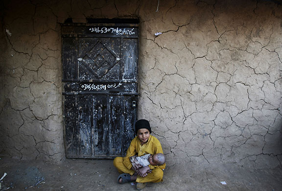 24 hours: Rawalpindi, Pakistan: An Afghan refugee youth sits holding a baby