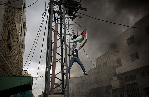 24 Hours in Pictures: A Palestinian climbs an electricity pole as he waves a flag during clashes