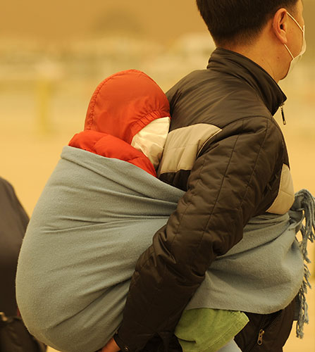 Sandstorms in China: A man carries a baby wrapped up against a sandstorm in Beijing