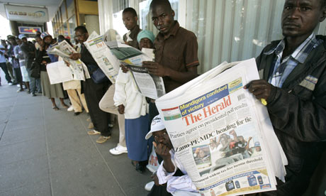 Harare residents read newspaper while they wait in a bank queue