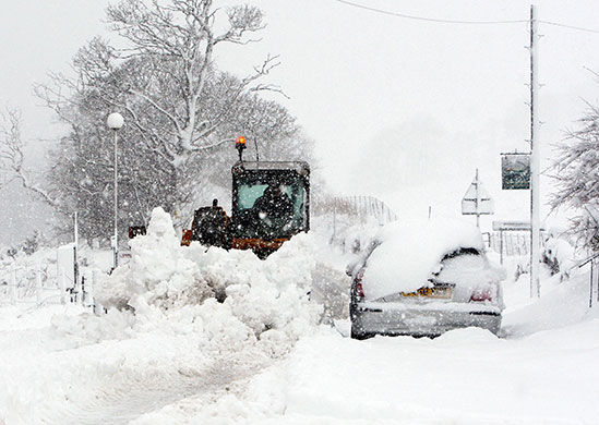 Snow in Scotland: A farmer clears snow from the main street in Carronbridge     