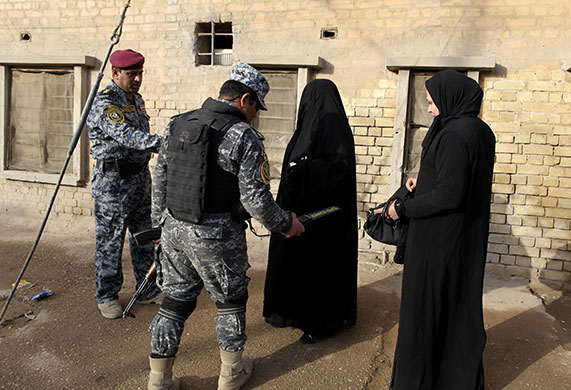 Iraq elections build up: Policemen search women passing near a polling station in Baghdad