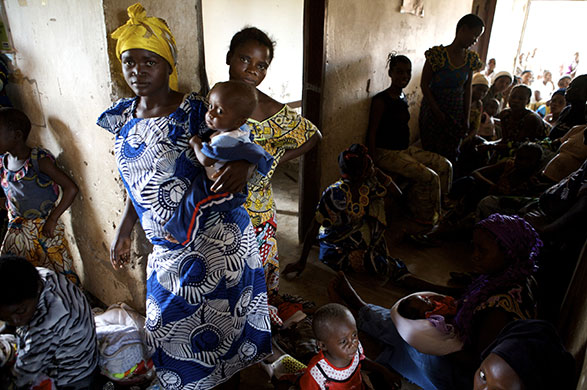 Women Health Workers: A woman and her baby stand in a busy Health Centre