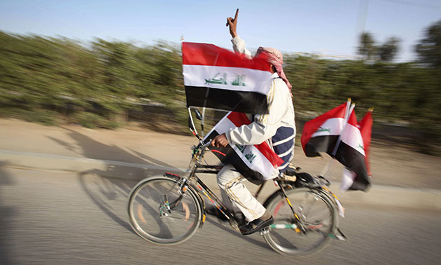 Elections in Iraq: A man on a bicycle covered with flags displays his inked finger