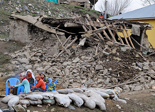 Turkey earthquake: A family waits among debris in front of a destroyed house in Okcular