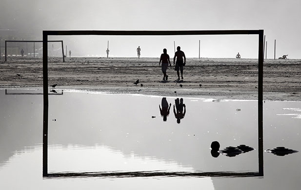 24 Hours in Pics: Residents walk near a soccer goal post on Copacabana beach after heavy rain