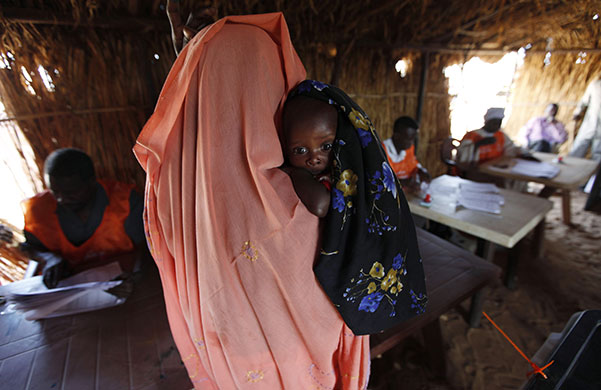 Sudan elections: A Sudanese refugee woman registers for voting while carrying a child