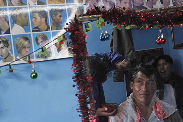 24 hours in pictures: El Alto, Bolivia: A man looks to pictures of haircut styles in a barbers