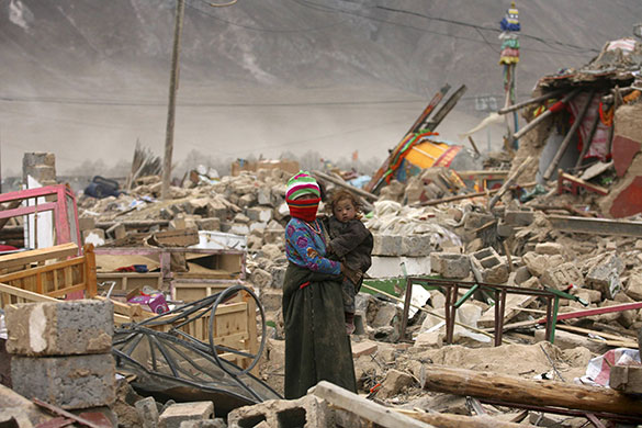 China earthquake: A woman carries her child by the ruins of her house in Gyegu