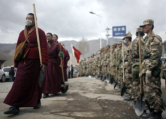 china quake mourning: Tibetan monks carrying shovels walk beside a row of paramilitary policemen