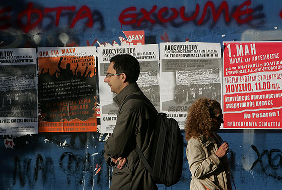 Week in Business: Pedestrians walk past posters in Athens