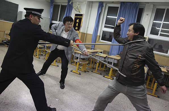 China school violence: Police officers demonstrate with a teacher the use of defensive steel forks