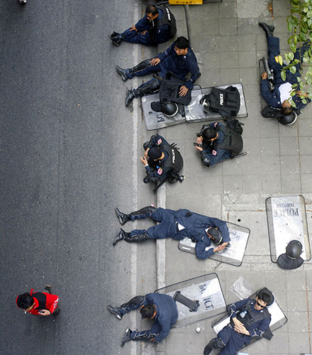 Thailand protests: Thai riot policemen rest as a red shirt supporter walks past
