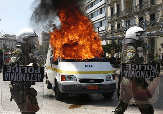 Athens Riot: Police in front of a burning television van during riots in Athens