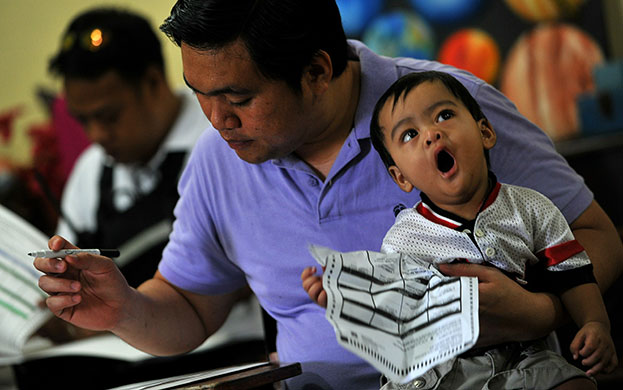 Philippine elections: A Filipino baby boy yawns as his father fills in his ballot