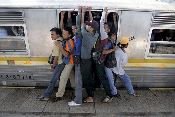 24 hours in pictures: Jakarta, Indonesia: Men struggle to board a packed commuter train