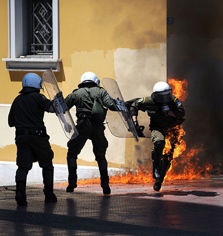 May Day protests: Athens, Greece: A riot policeman runs away from a fire