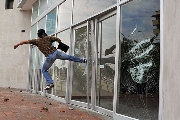 May Day protests: Cali, Colombia: A demonstrator smashes a glass door of the office of a bank