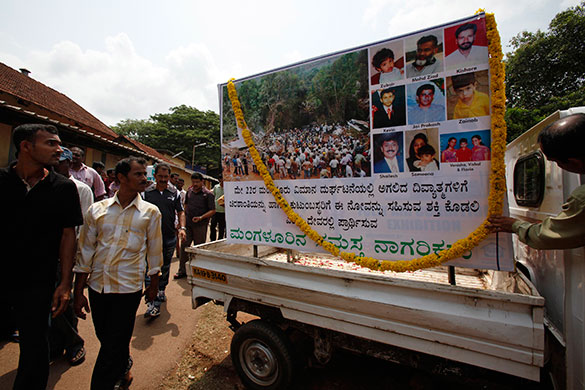 Air India plane crash: People walk past a board displaying pictures of the spot and the victims