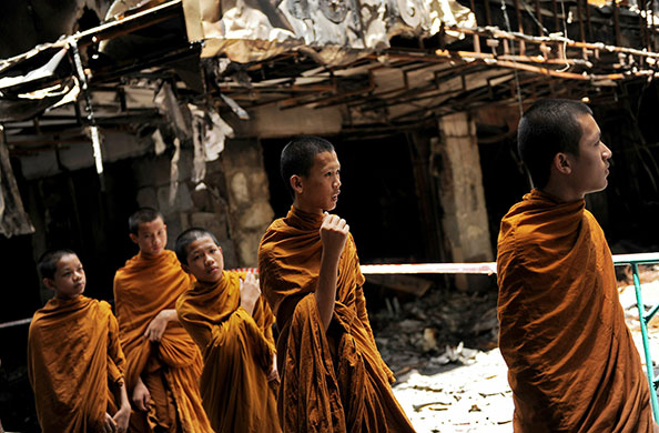 24hours: Buddhist monks walk past burnt shops, days after a Thailand army assault