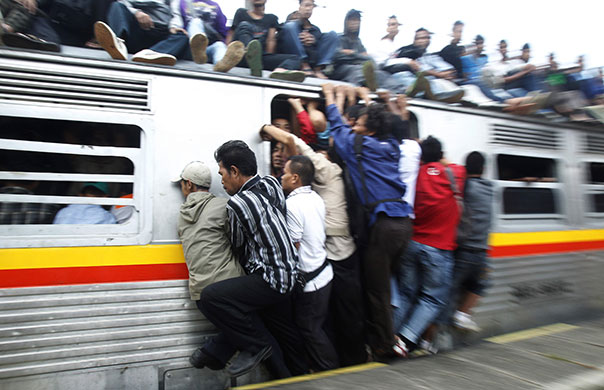 24 hours: Depok, Indonesia: People hang on to a door on a commuter train 