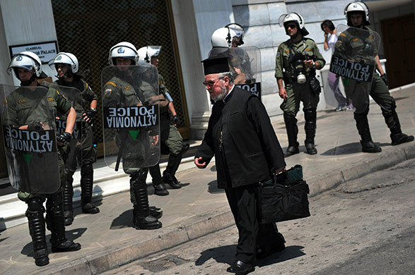 Greece: An Orthodox priest walks past riot policemen